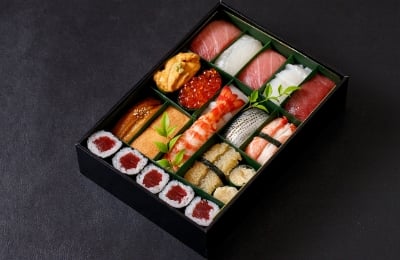 高級感ある黒の四角い箱に、赤身、光物、うに、蒸しエビ、いくらなどの握り寿司15貫と細巻が1本分がセットで詰められている写真